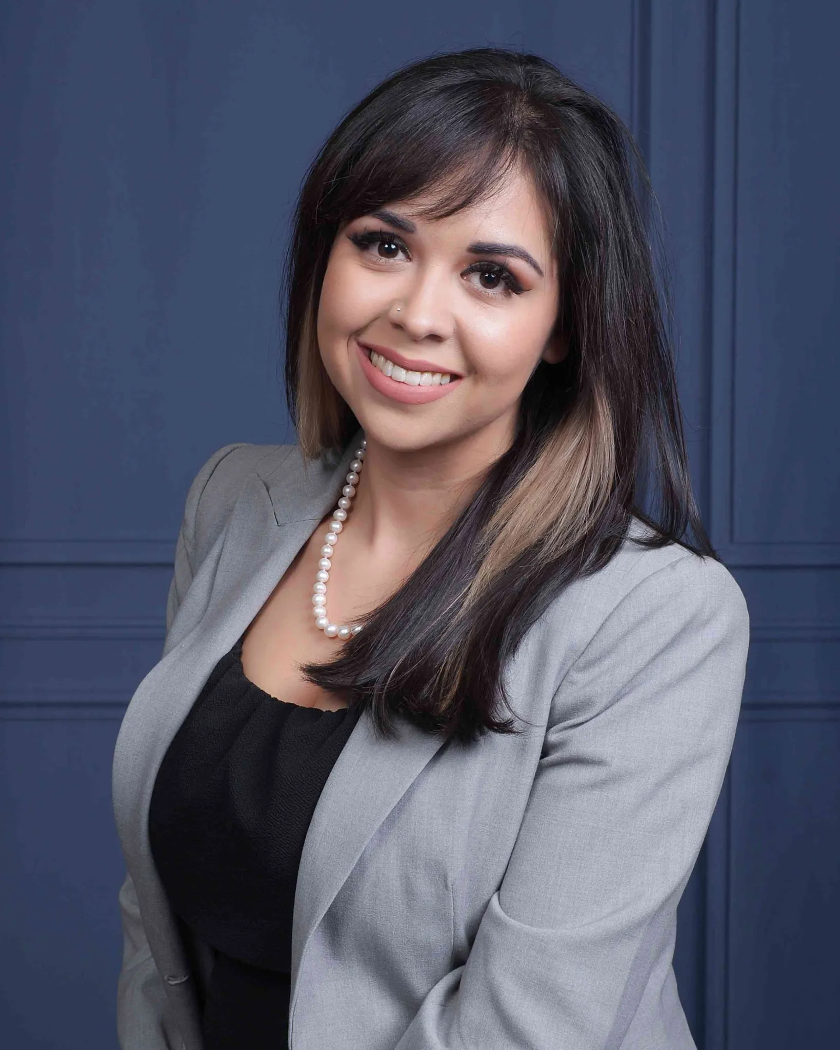 Gina Quintanilla sonriendo, con saco gris y collar de perlas